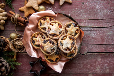 Mince pies in a vintage old plate with christmas decoration on wooden background. Traditional Christmas baking.