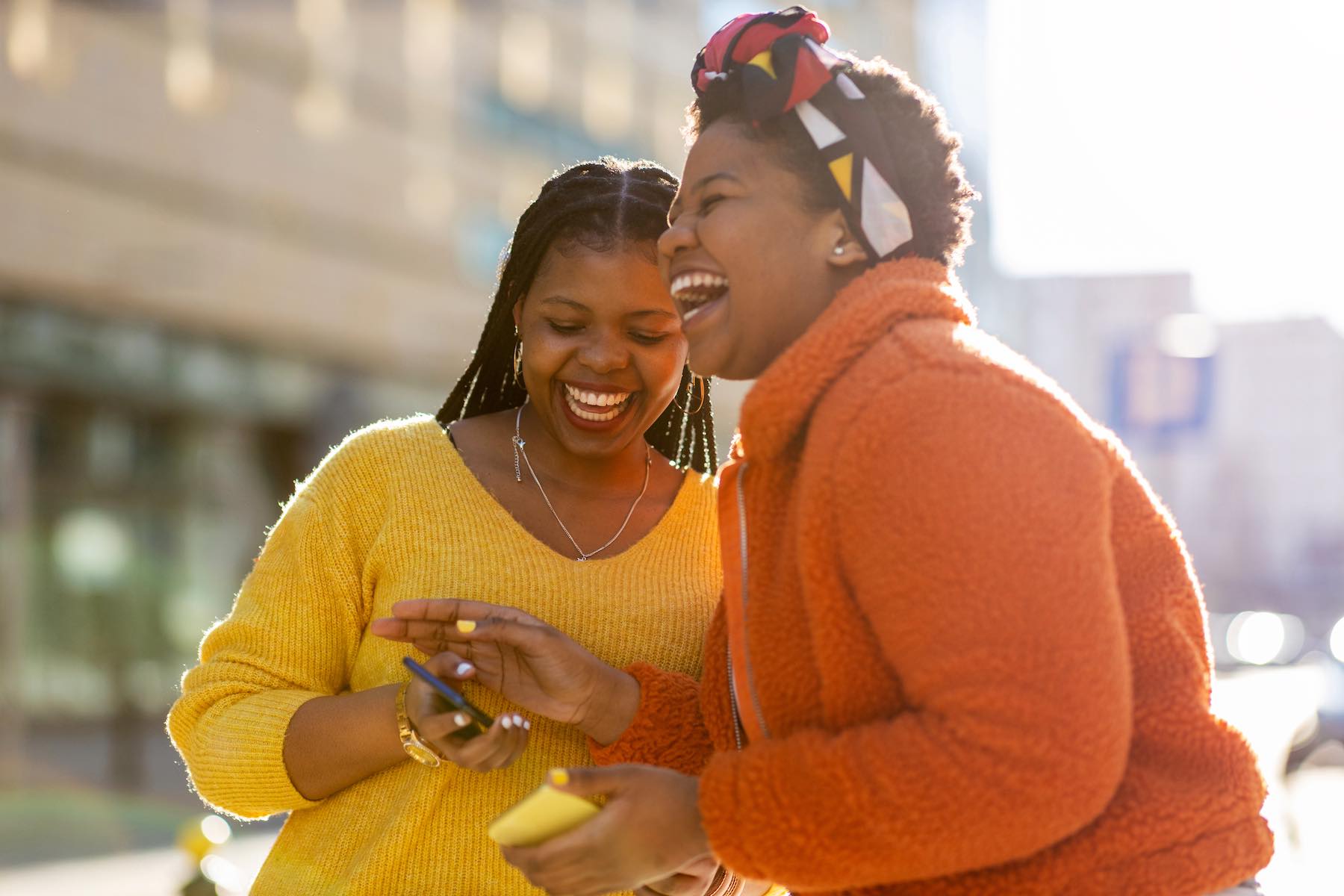 Happy female friends sending messages with their smartphones in the city