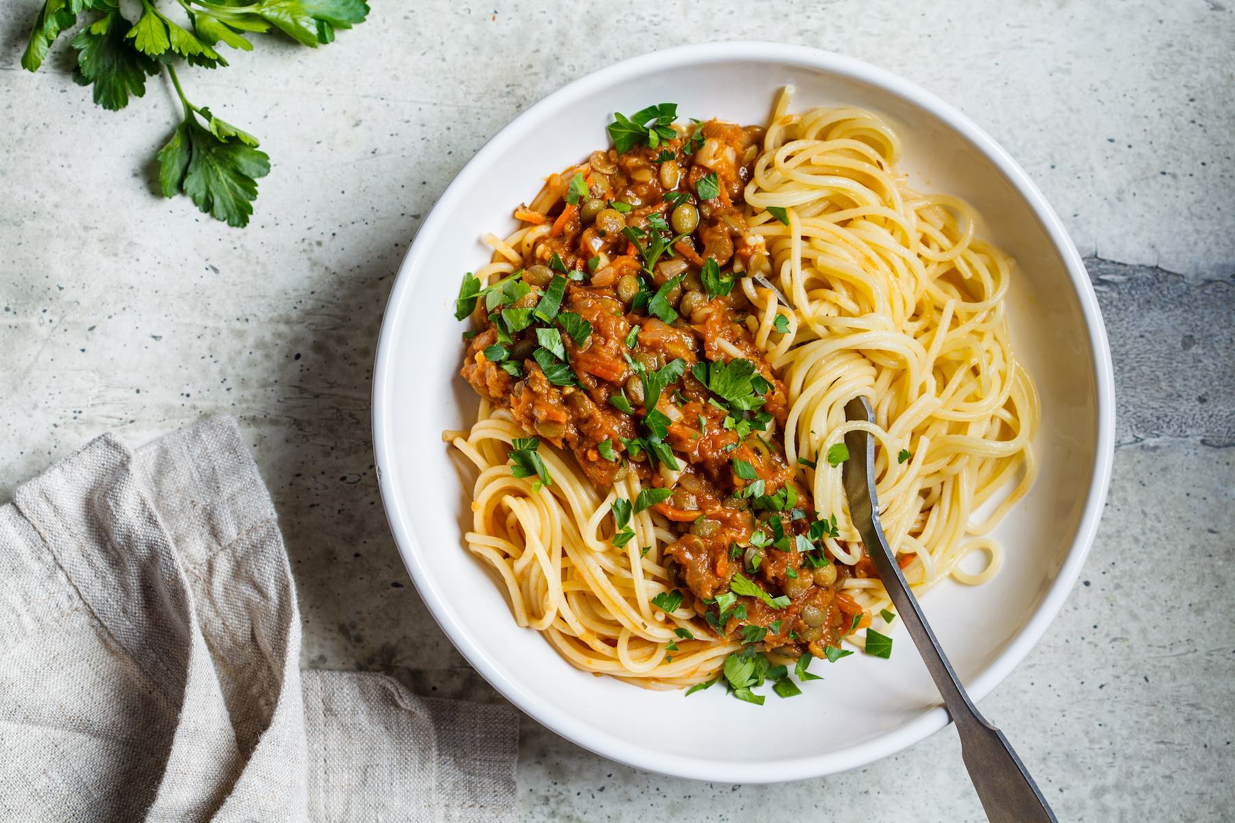 Vegetarian lentils bolognese pasta with parsley in a white dish. Healthy vegan food concept.