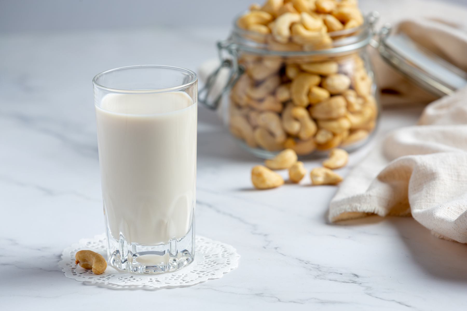Vegan cashew milk in glass with cashews nuts on marble background